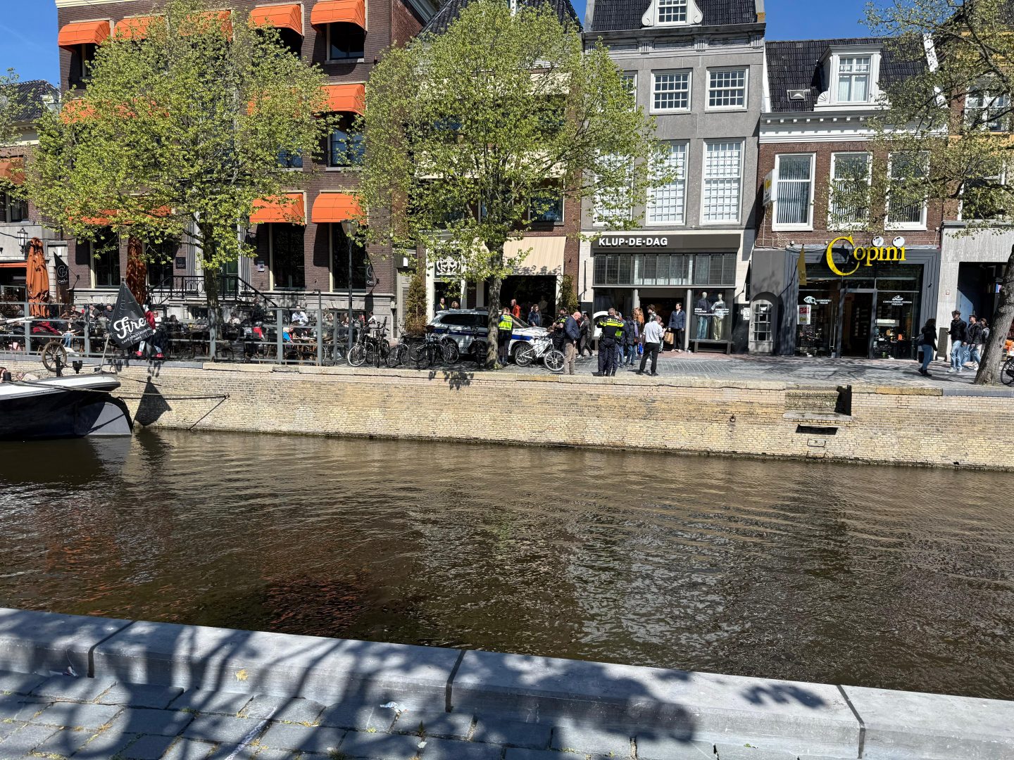 Jongeman op terras red vrouw op scootmobiel uit stadsgracht